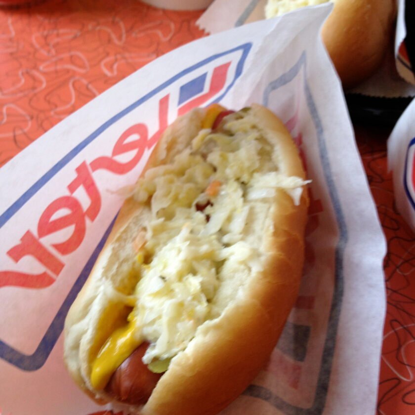 A hot dog rests in a paper wrapper, generously topped with shredded sauerkraut and mustard.